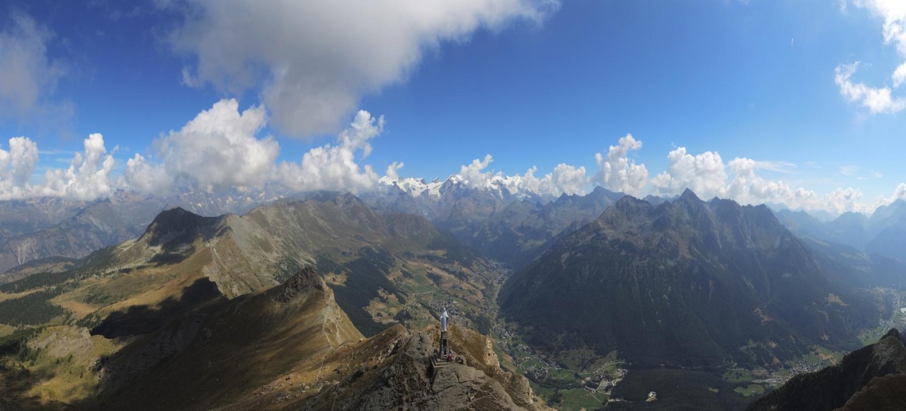 Panoramica aerea a 180° da sud-ovest, si riconosce l’ultimo tratto di sentiero a sinsitra della statua, nonché quello proveniente da Promiod a sinistra e l’uscita dalla Via delle Roccette a destra